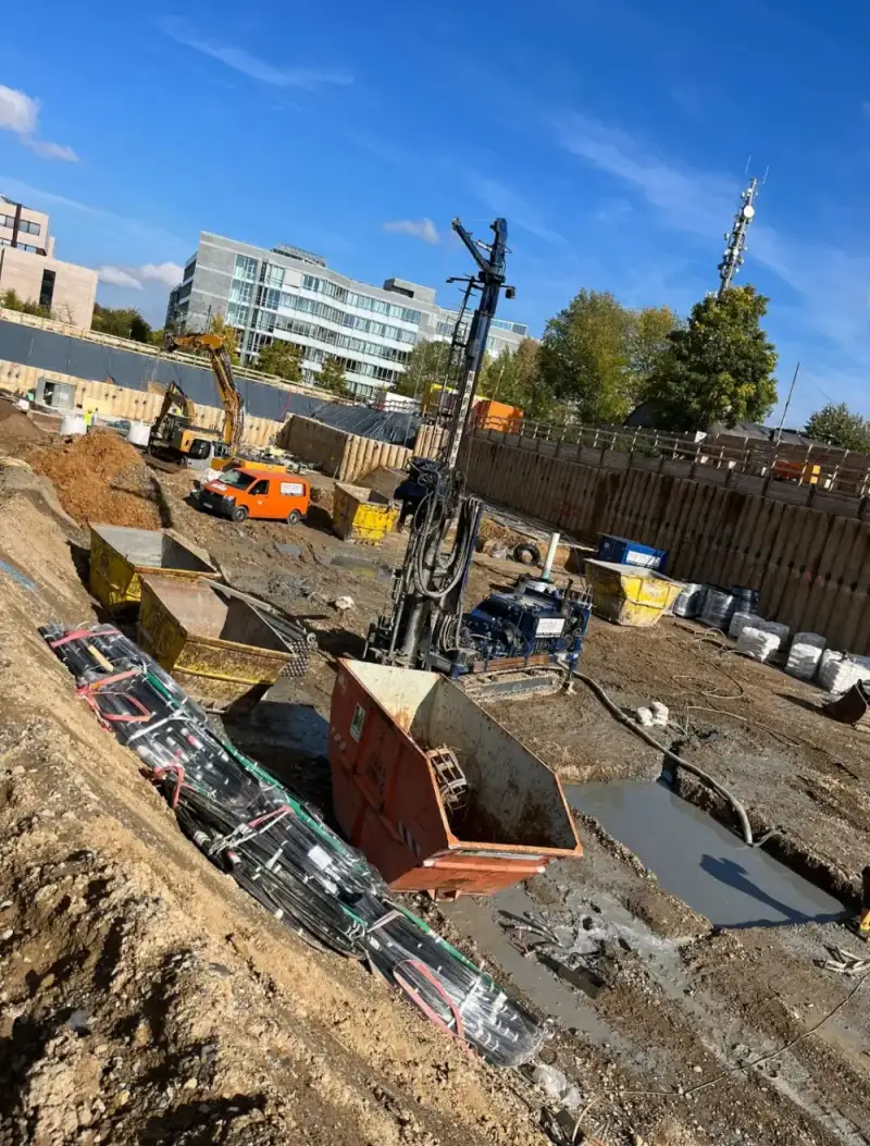Bohrgerät und Container in einer Baugrube, dahinter Bürogebäude und ein Bagger